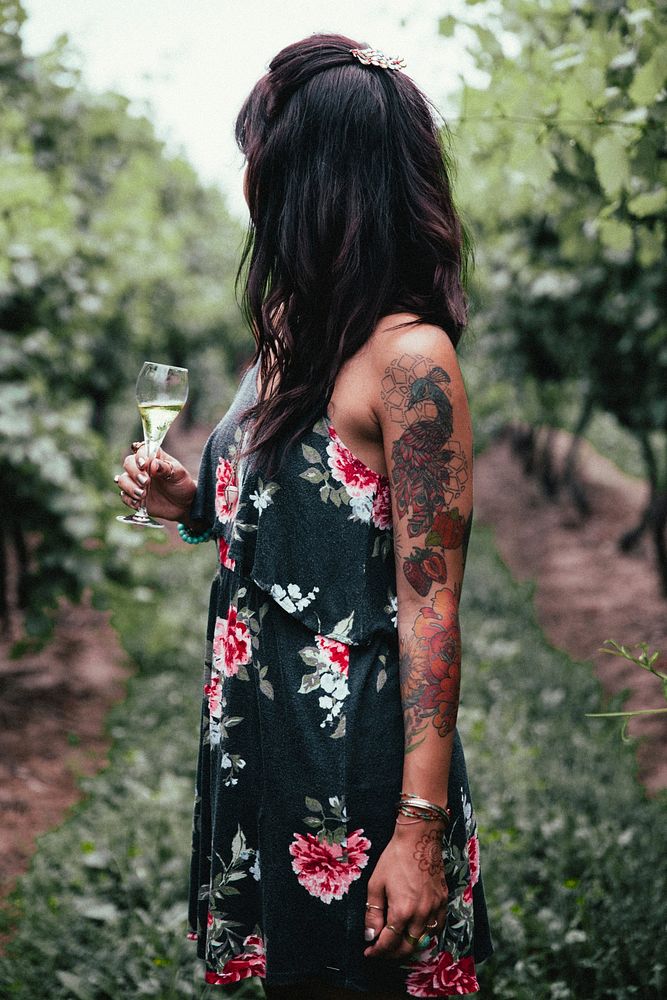 A young tattooed woman enjoying a glass of winewhile standing in a vineyard where it all began