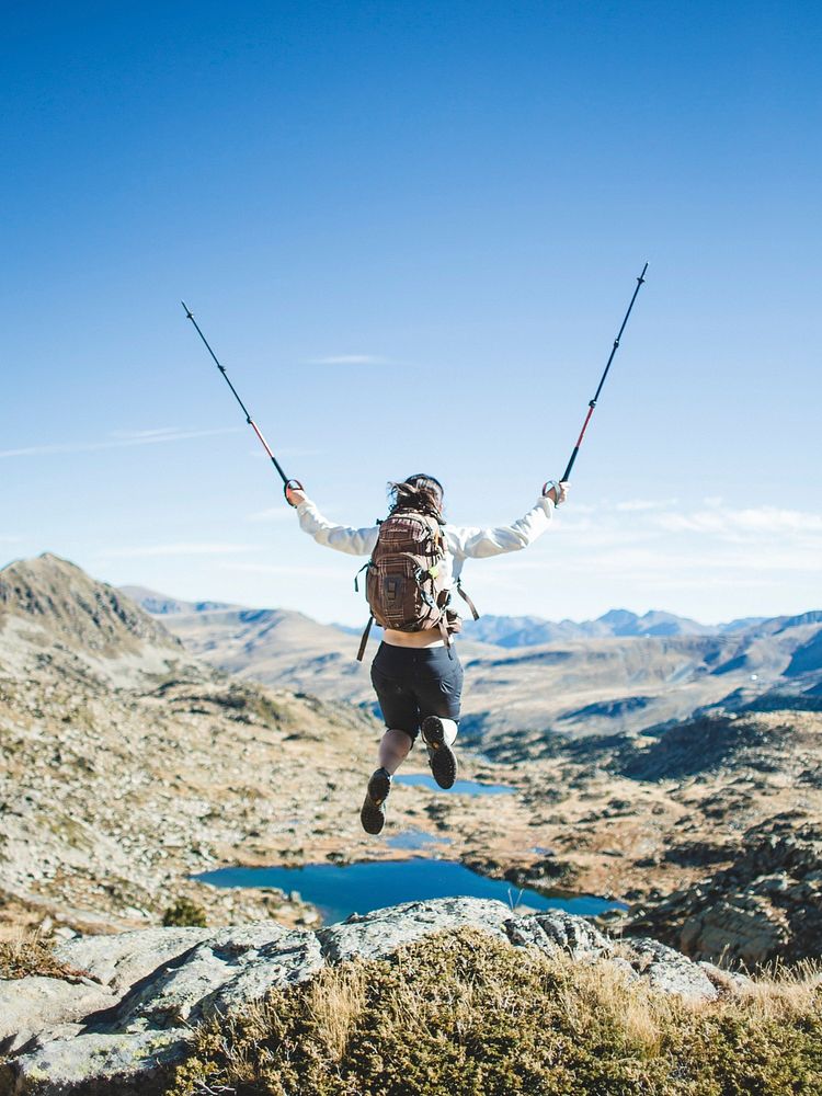 Woman hiker with backpack and trekking poles jumping in the air image,