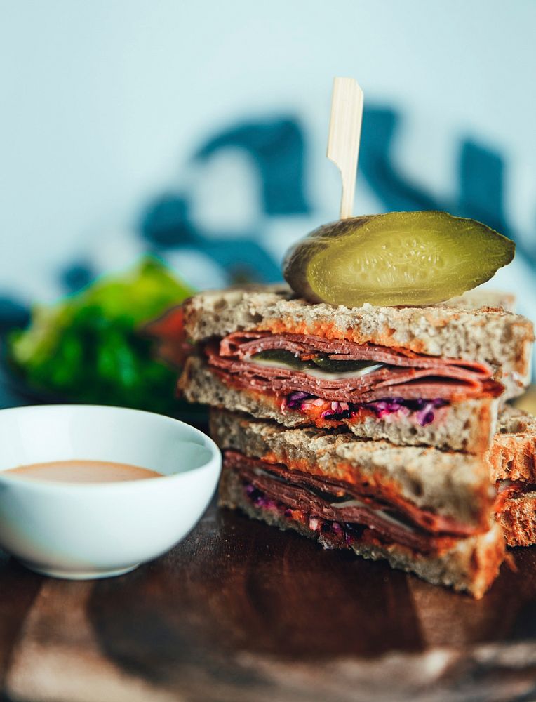 Free halved and stacked salami sandwich with a pickle on top and a bowl of dipping sauce photo, public domain food CC0 image.
