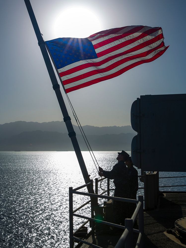 U.S. Sailors attached to the amphibious assault ship USS Kearsarge (LHD 3) lower the U.S. flag after getting underway from…