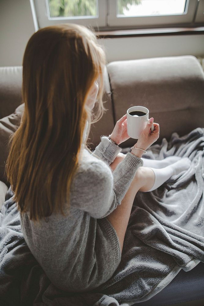 Free woman sits on the sofa drinking coffee photo, public domain CC0 image.