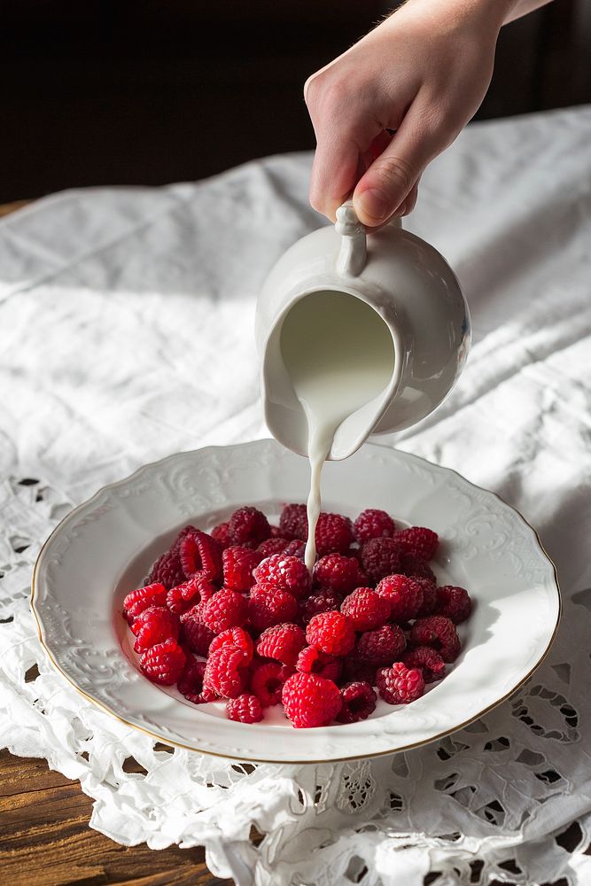 Free closeup milk being poured into a plate full of bright red raspberries, food public domain photo. 