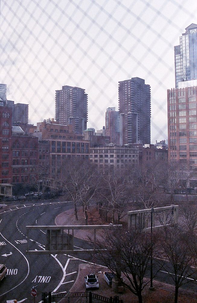 View of chain link fence with city buildings and roads in the background