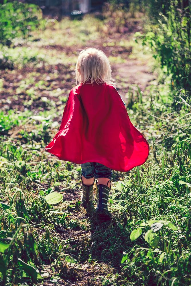 Little superhero walking in a field