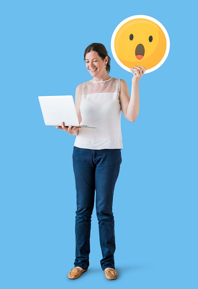 Woman holding a surprised emoticon and using a laptop
