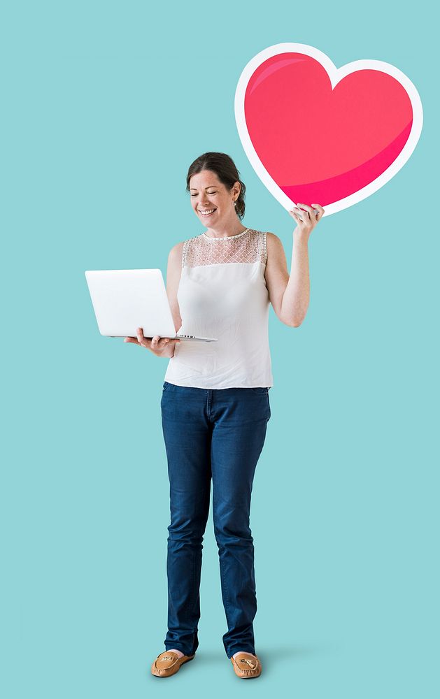 Standing woman holding a heart emoticon and a laptop