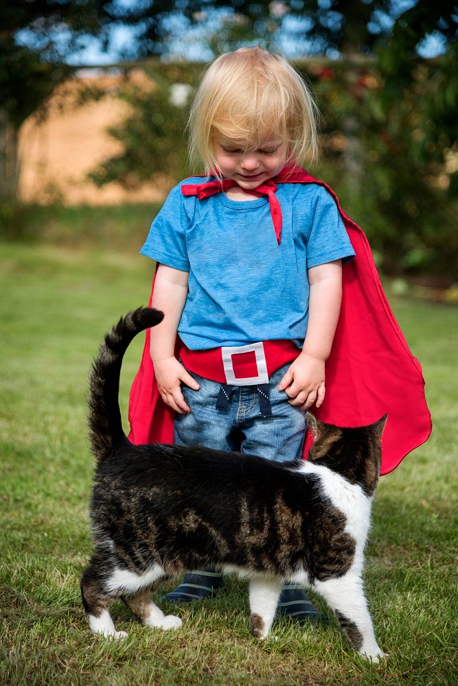 Little boy in superhero costume with his cat in a yard