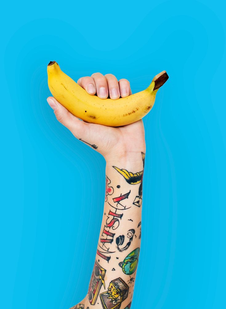 Tattoo covered arms holding a banana