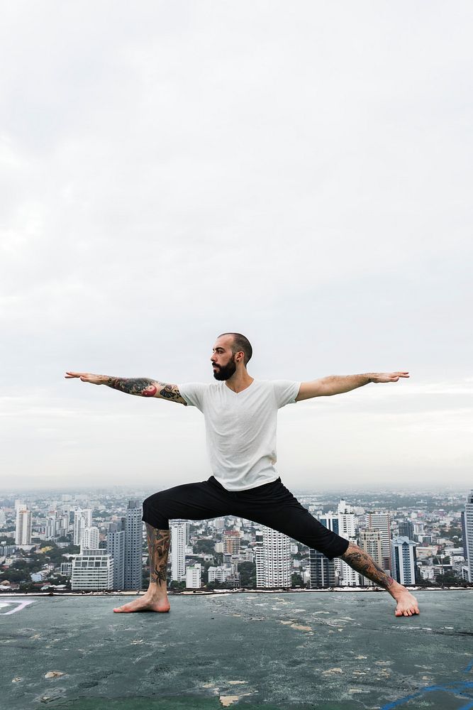 Man practicing yoga on the rooftop and cityscape background