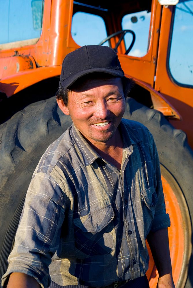 Mongolian farmer standing in front of his tractor reaching forward.