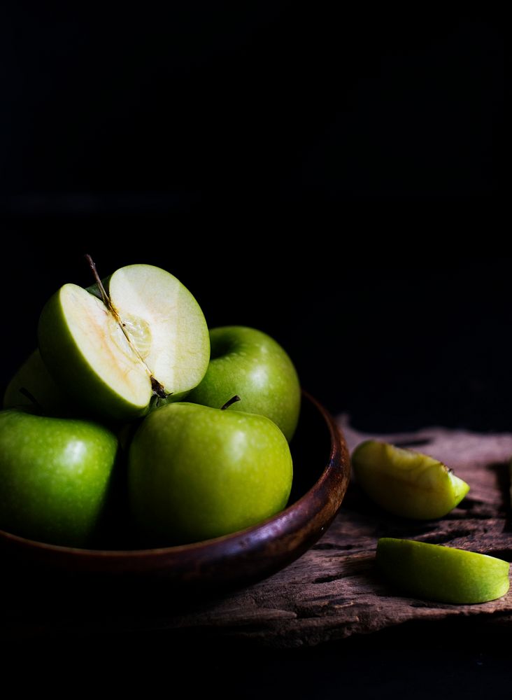 Closeup of fresh cut green apples in wooden bowl with black background