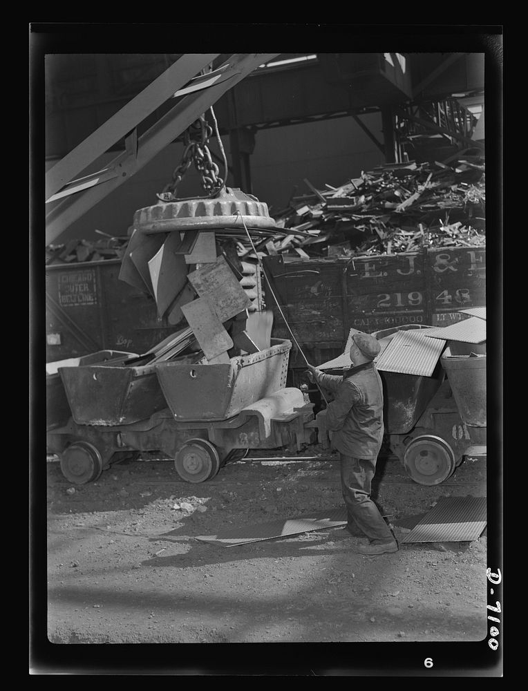 Salvage. Scrap for steel mills. A worker guides the magnet which unloads steel scrap from open freight cars to the waiting…