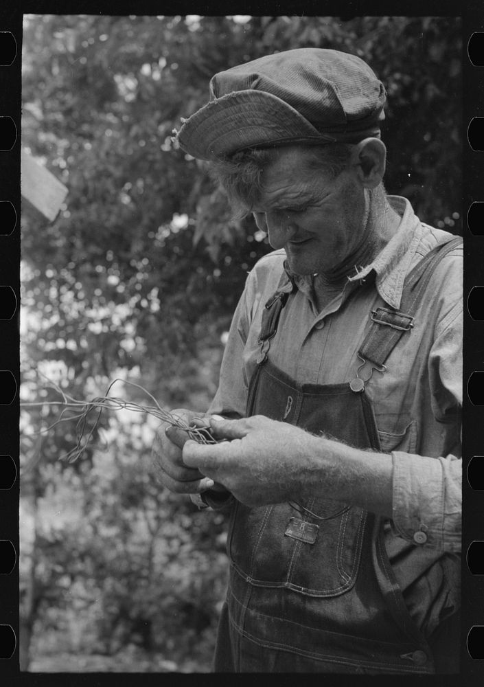 Elmer Thomas, migrant to California, trying to untangle a piece of wire so that he can wire some things onto his truck…