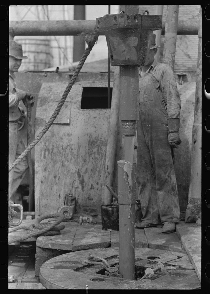 [Untitled photo, possibly related to: Roughnecks guiding bailer into hole during bailing out operations, oil well, near…