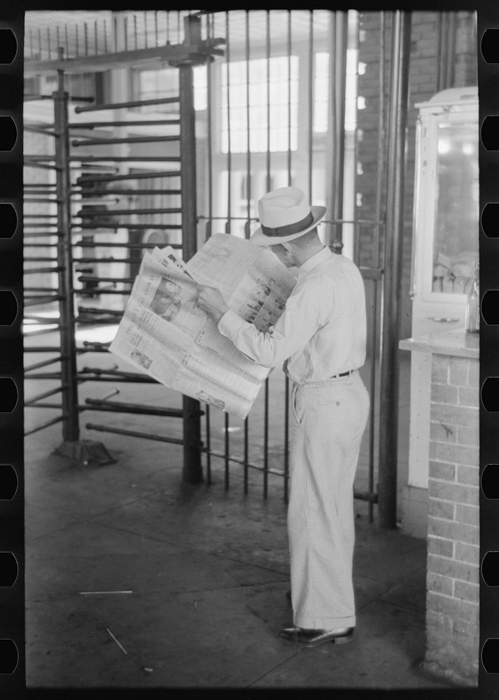 Man reading newspaper while waiting for streetcar. Streetcar station, Oklahoma City, Oklahoma by Russell Lee
