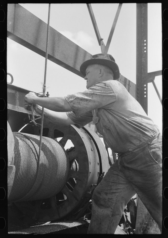 Roughneck tying piece of string around cable to determine depth to which bailer is being lowered. Oil well near Seminole…