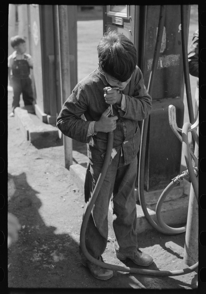 Mexican migrant boy drinking out of water hose at filling station where the truck which is taking him home from Mississippi…