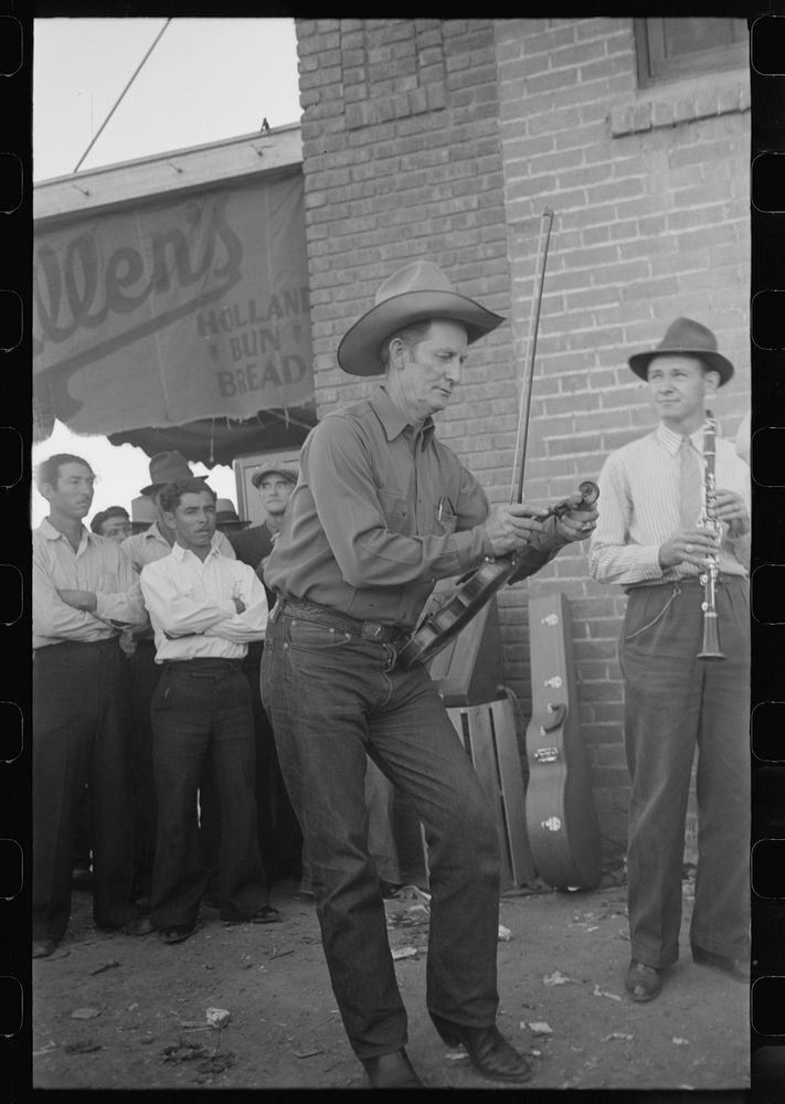 Member of orchestra which plays outside grocery store on Saturday afternoon tuning his violin, Phoenix, Arizona by Russell…