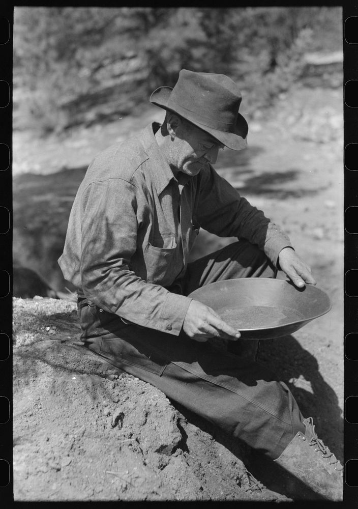 Gold prospector examining a pan to see how much gold it contains. Pinos Altos, New Mexico by Russell Lee