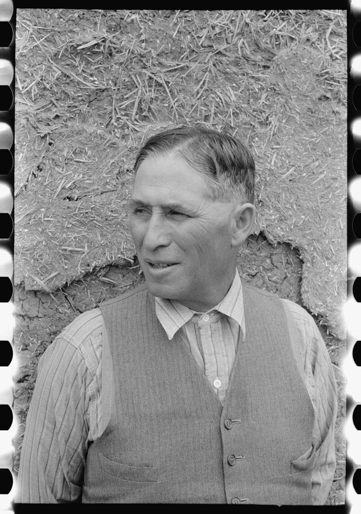 Spanish-American farmer standing in front of adobe wall, Chamisal, New Mexico by Russell Lee