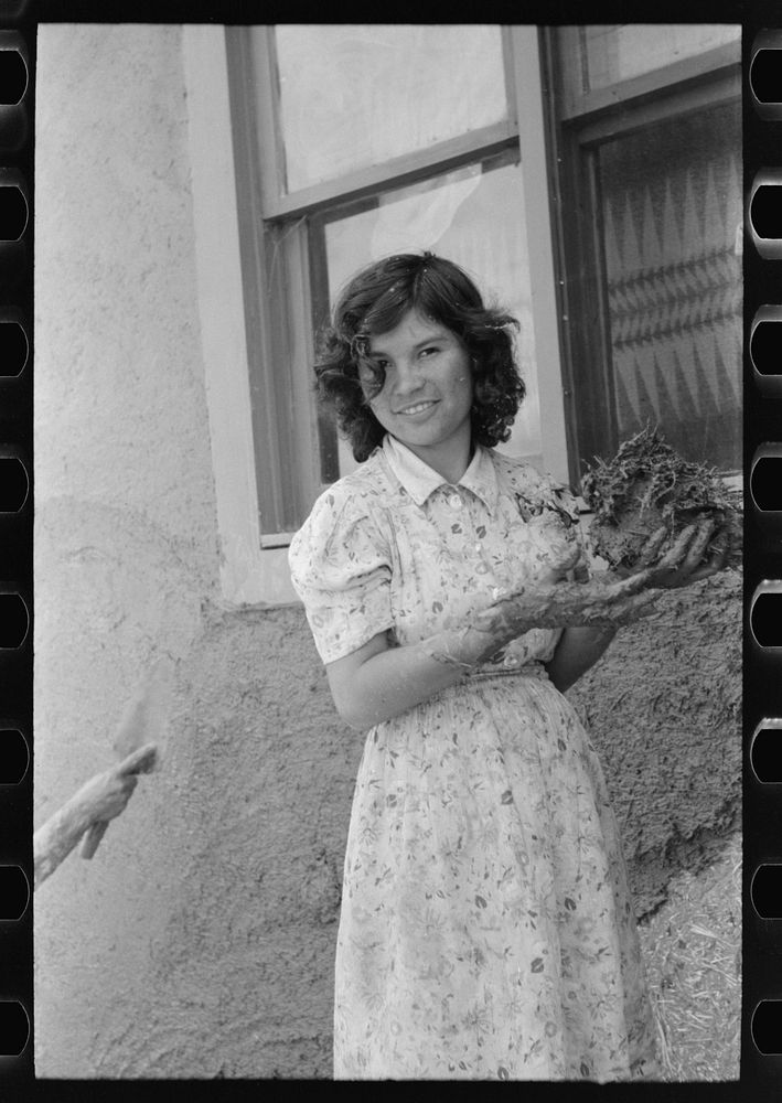 Spanish-American girl with handful of adobe plaster, Chamisal, New Mexico by Russell Lee