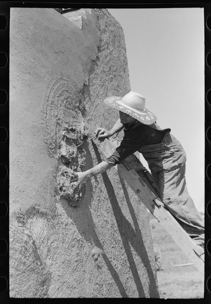 Spanish-American woman plastering adobe house, Chamisal, New Mexico by Russell Lee