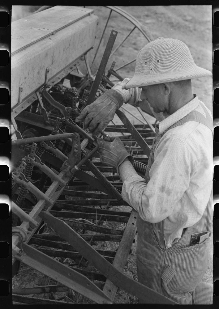 Mormon farmer working on FSA (Farm Security Administration) cooperative drill, Oneida County, Idaho. While the members of…