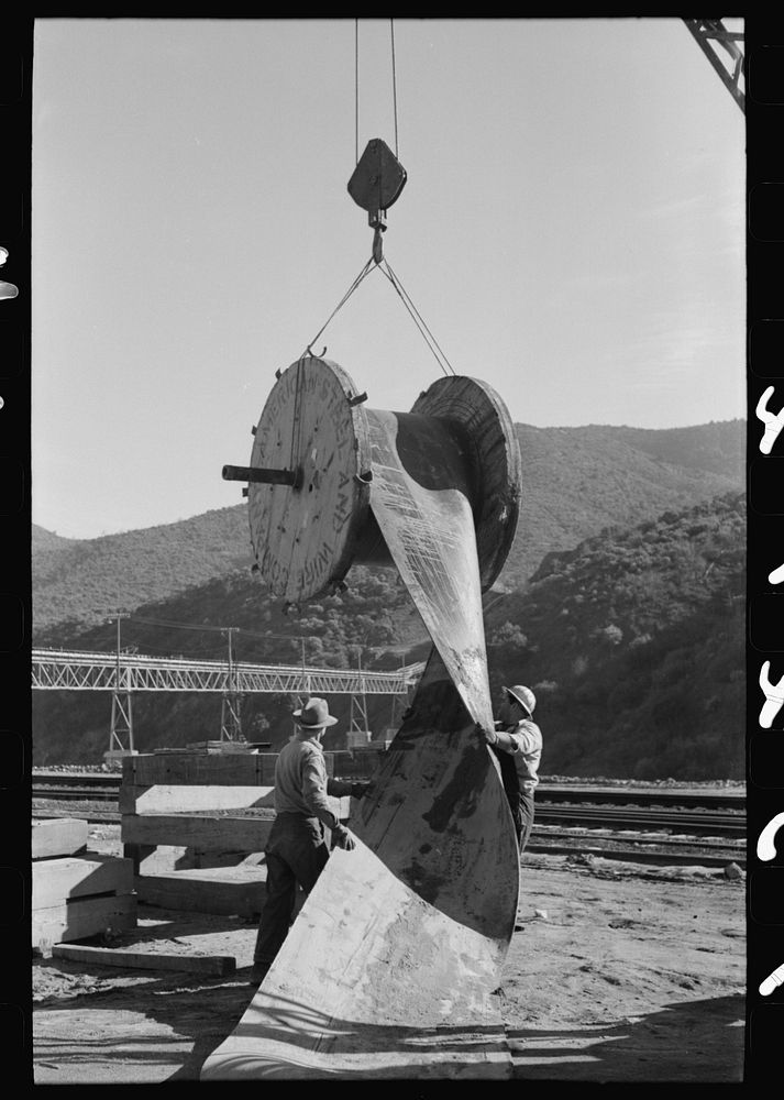 Workmen handling section of rubber conveyor belt which transports gravel to Shasta Dam, Shasta County, California by Russell…
