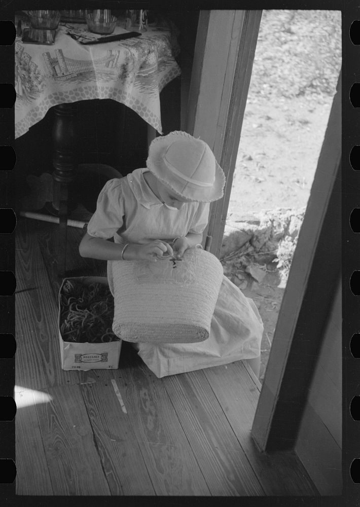 French Village, a small settlement on St. Thomas Island, Virgin Islands. Young girl embroidering a straw basket to be sold…