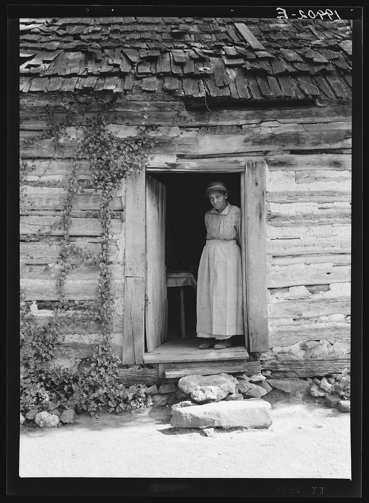Caroline Atwater standing in the kitchen doorway of double one and a half story log house. North Carolina. Sourced from the…
