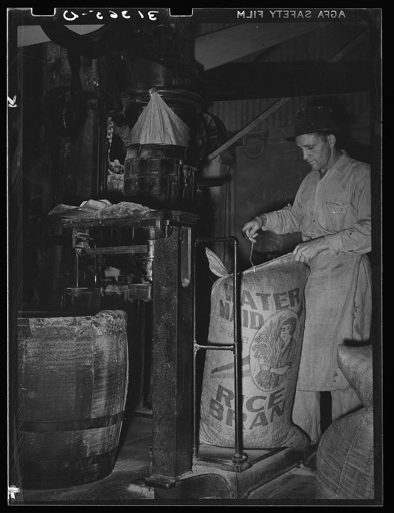 Sewing bag of rice brand after being weighed in rice packaging process. Crowley, Louisiana by Russell Lee