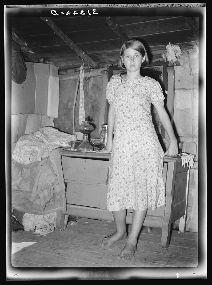 Girl standing in front of bureau in shack home. Tin Town, Caruthersville, Missouri by Russell Lee