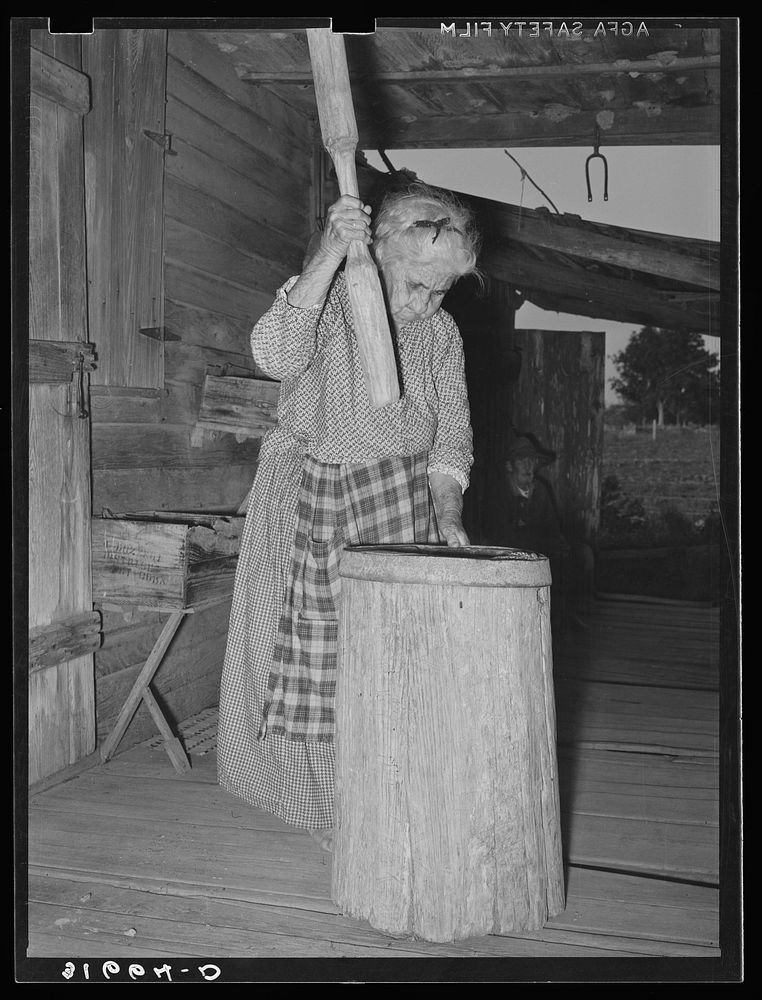 Aged Cajun woman using crude mortar and pestle in process of hulling rice. Near Crowley, Louisiana by Russell Lee