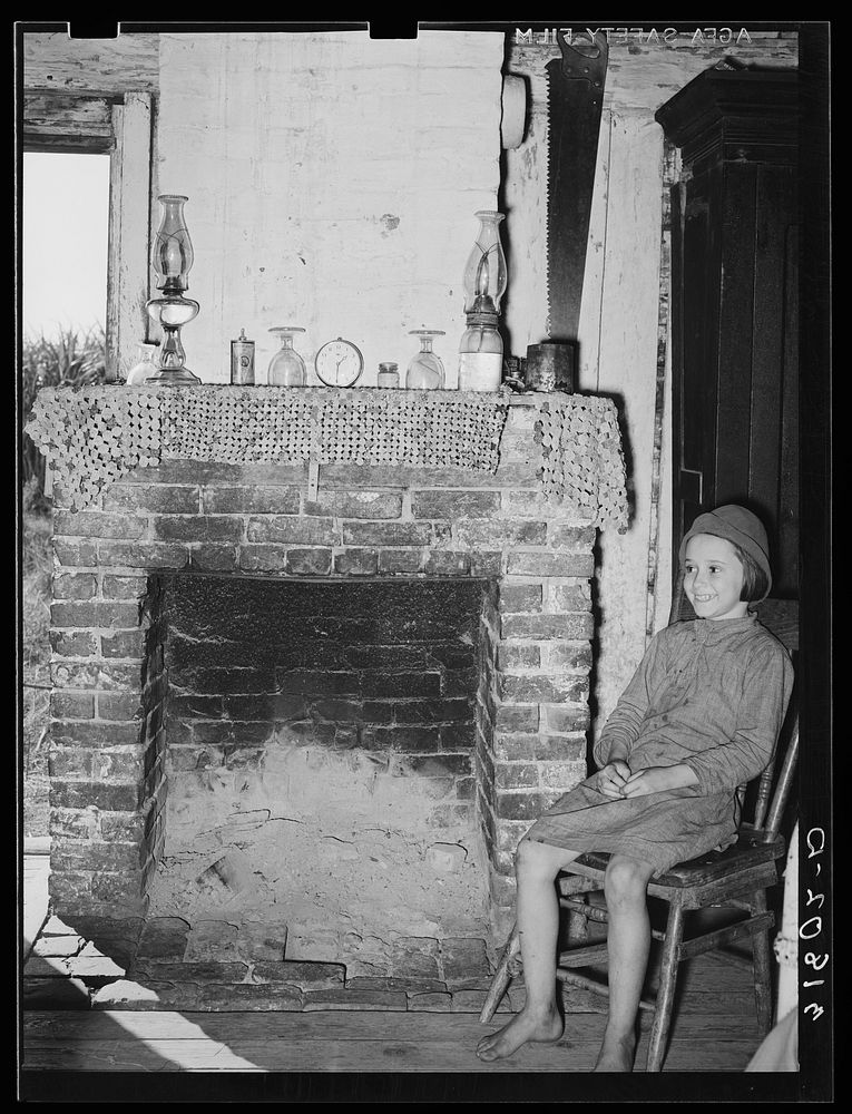 [Untitled photo, possibly related to: Daughter of Cajun day laborers sitting in front of fireplace in home near New Iberia…