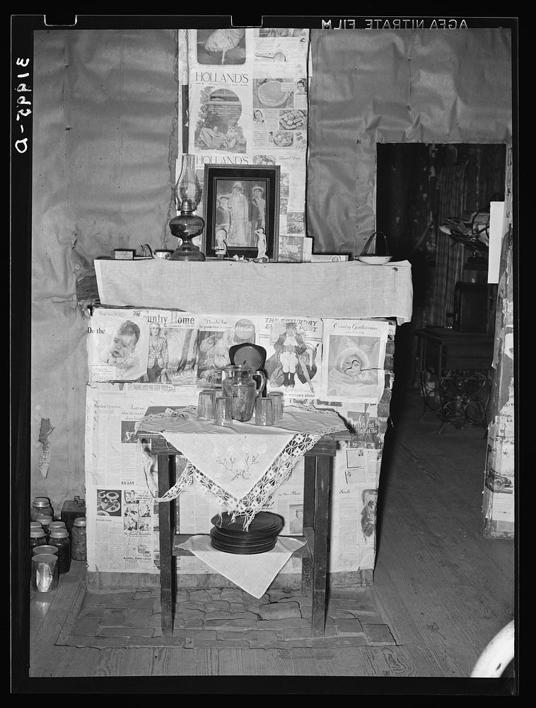 Fireplace closed with screen decorated with newspapers in temporary home of FSA (Farm Security Administration) clients near…