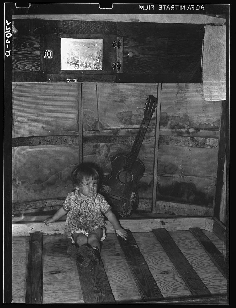 Child of migrant parents sitting on drop bed in trailer home. Weslaco, Texas by Russell Lee