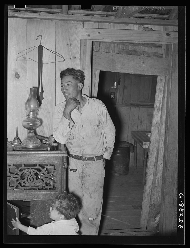 Mexican labor contractor and child in their home. Notice that the doorway shows the construction of the house. Two houses…