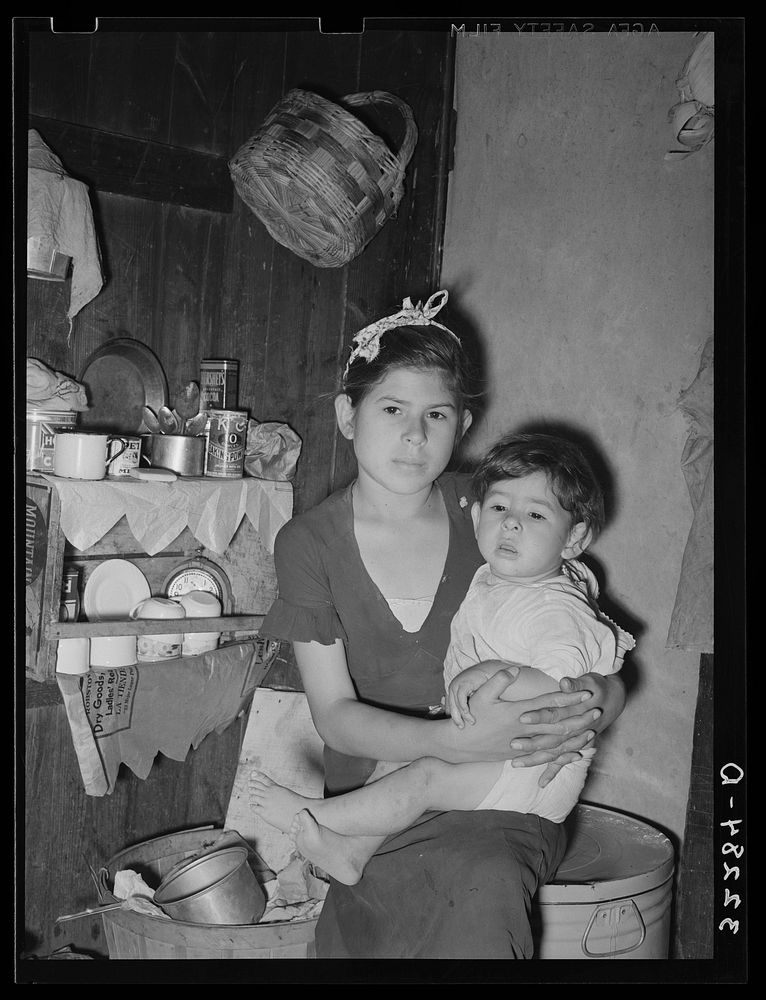 Mexican girl with baby brother in corner of room in which the entire family lives. Robstown, Texas by Russell Lee