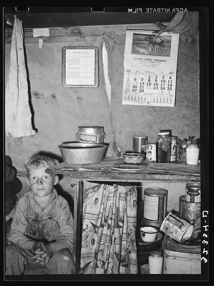 Child of migrant sitting by kitchen cabinet in tent home near Edinburg, Texas by Russell Lee