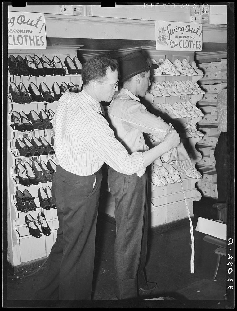 Clerk measuring a customer for a suit of clothes. San Augustine, Texas by Russell Lee