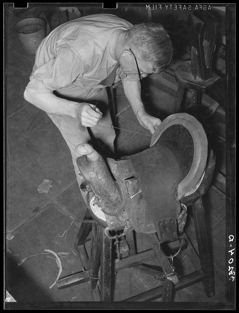 Saddle maker sewing in repairing saddle. Notice awl in his hand. Saddle shop, Alpine, Texas by Russell Lee