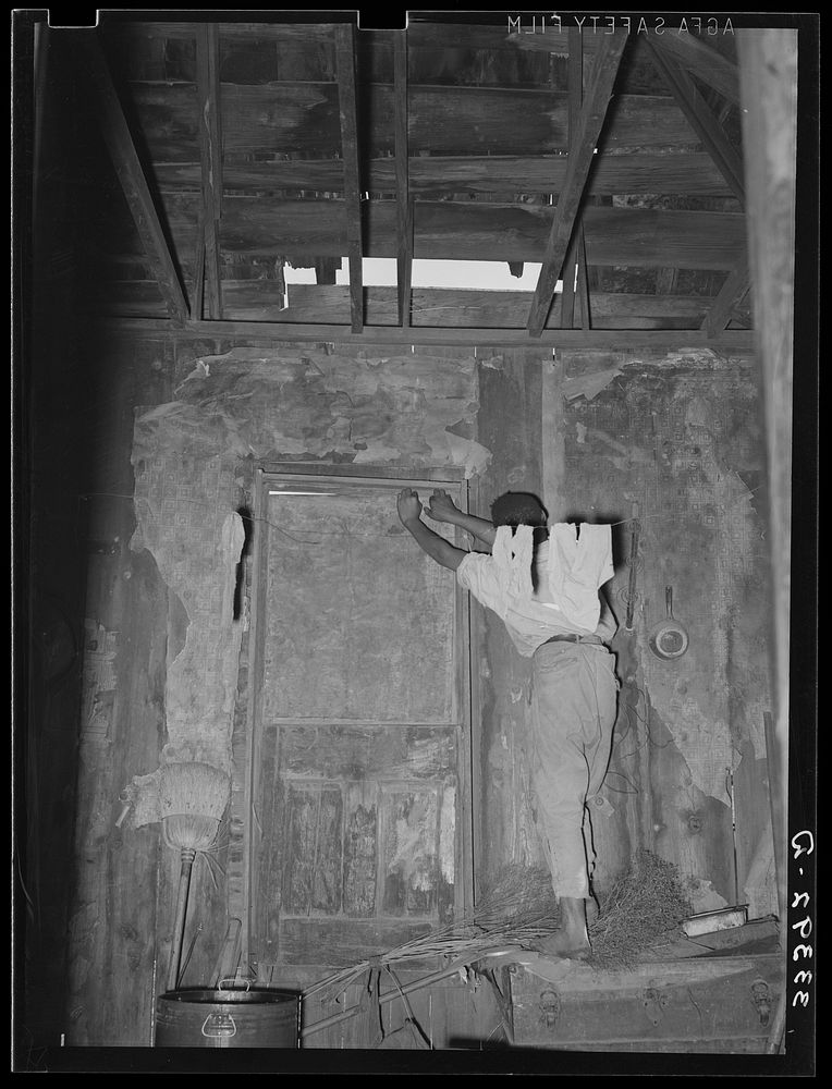 [Untitled photo, possibly related to: Room in house of  agricultural day laborer. Note hole in roof and boarded-up door.…