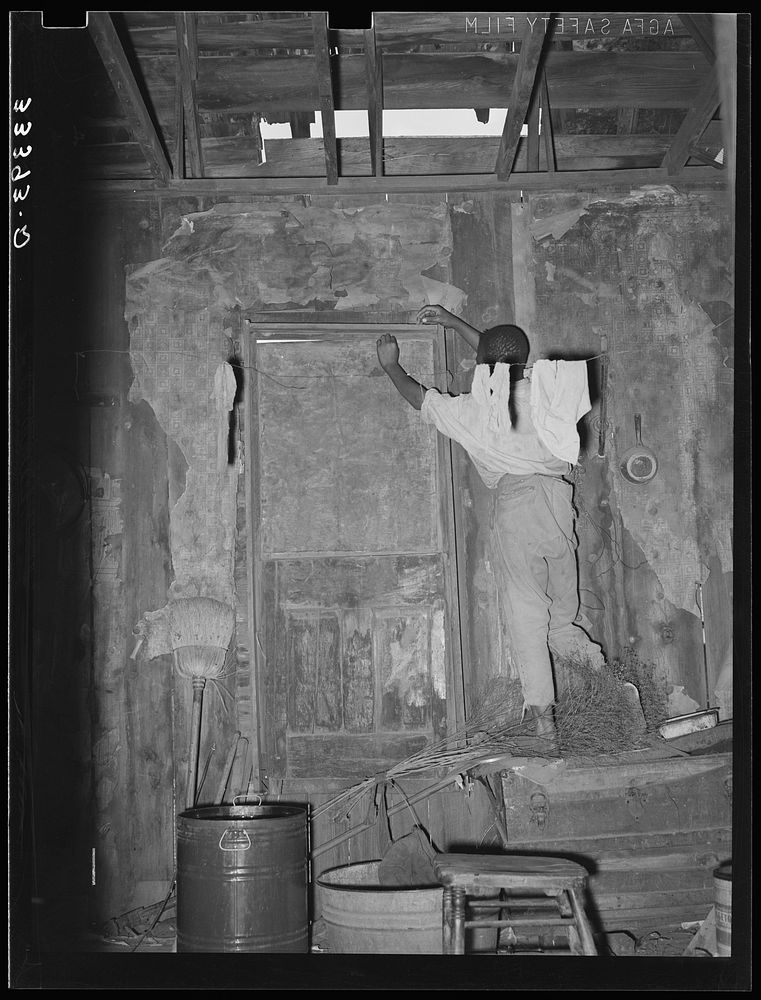 Room in house of  agricultural day laborer. Note hole in roof and boarded-up door. Muskogee County, Oklahoma by Russell Lee