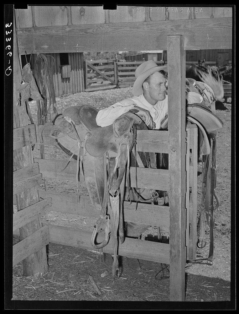 Cowboy leaning on saddle. Saddle room on SMS Ranch near Spur, Texas by Russell Lee
