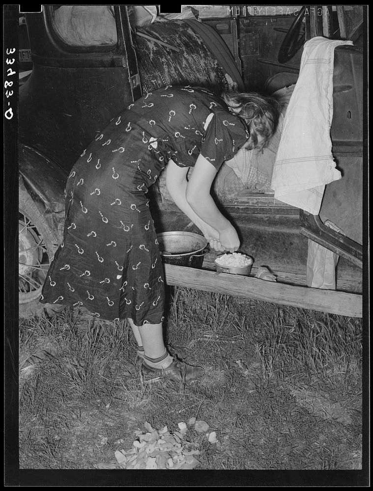 [Untitled photo, possibly related to: Migrant woman peeling potatoes on running board of car while camped near Prague…
