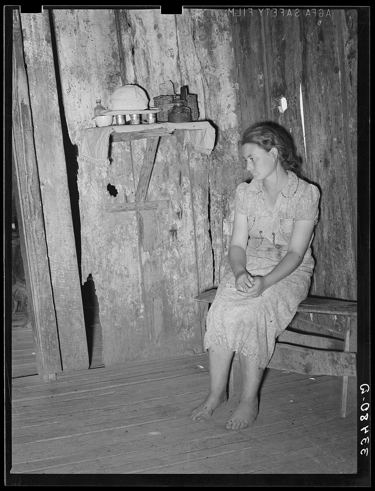 Agricultural day laborer sitting in corner of one room of her two-room shack home near Webbers Falls, Oklahoma. This girl…