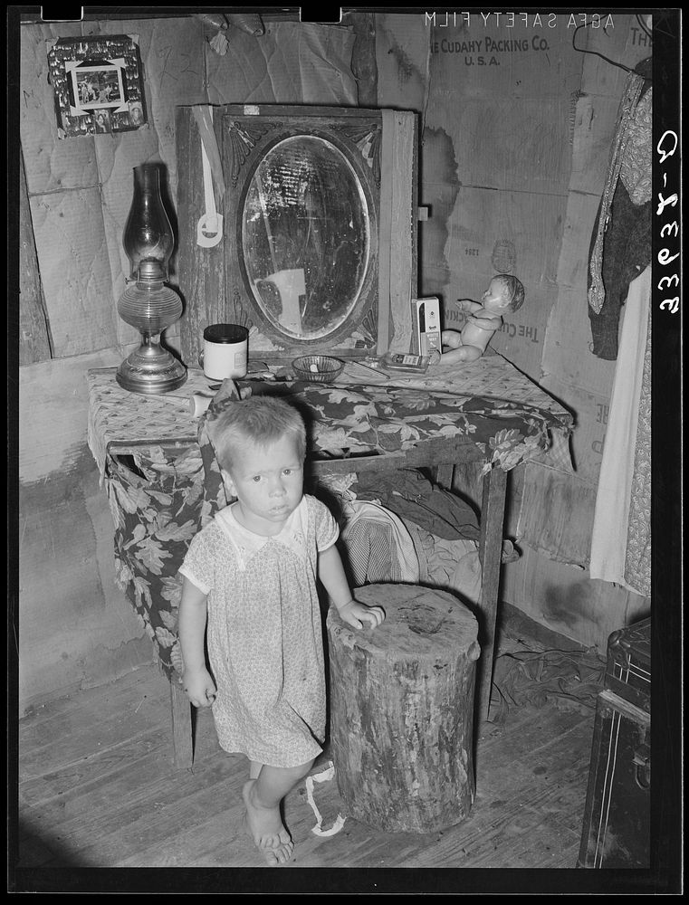 Child of agricultural day laborer in front of dressing table in shack. Near Vian, Oklahoma by Russell Lee