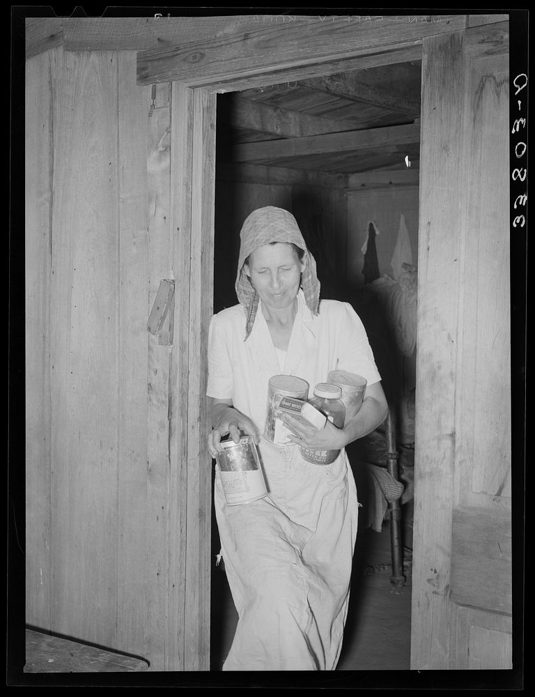 Mrs. Elmer Thomas, migrant to California, removing the spices, coffee, etc., to their car from their home which they are…