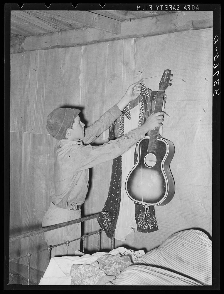 Migrant boy removing guitar before they leave for California. At old homestead near Muskogee, Oklahoma by Russell Lee