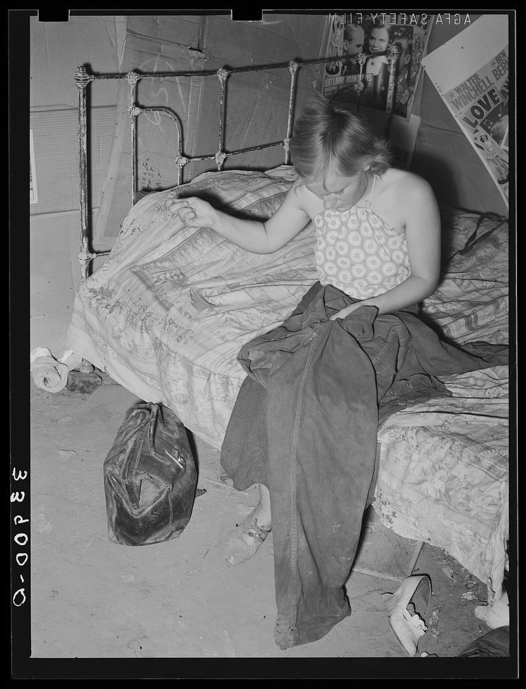 Young married girl living in Mays Avenue camp patching her husband's overalls. Oklahoma City, Oklahoma by Russell Lee